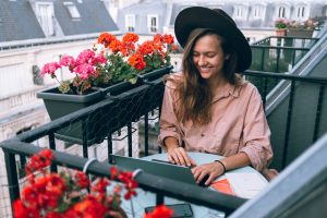 Kvinde sidder på terrasse med hat og computer