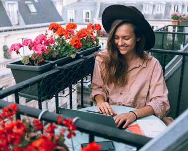 Kvinde sidder på terrasse med hat og computer